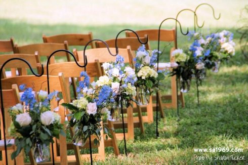 Mason jars were equipped with wire hangers, filled with small floral bouquets, and hung from shepherds hooks at the end of each row of chairs.